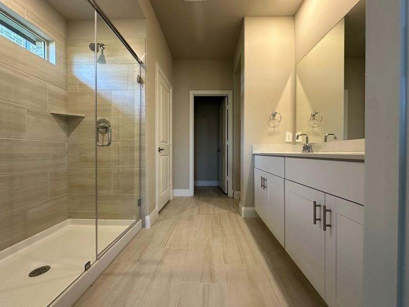 Bathroom featuring a walk-in shower with glass enclosure, integrated shower niche, and a dual-sink vanity with white cabinetry and chrome hardware