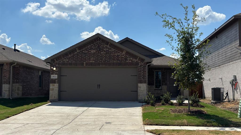 Brick facade with stone accents, attached garage, concrete driveway, and landscaped front yard
