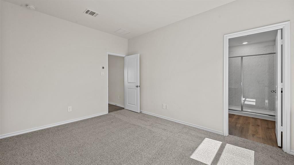 Carpeted flooring, neutral wall tones, and doorway access to an adjoining room with wood-finish flooring and a glass-enclosed shower