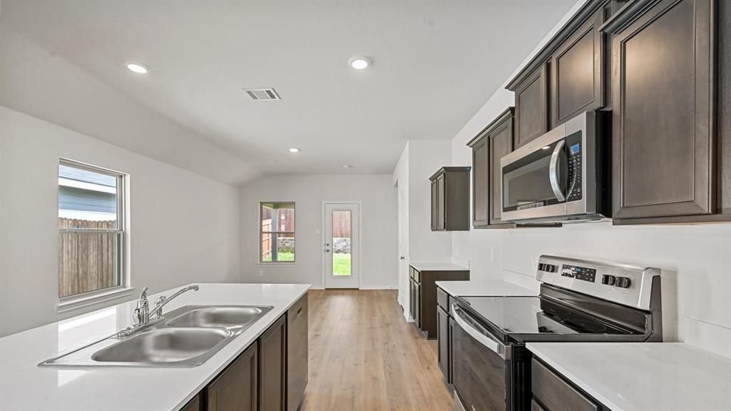 Kitchen featuring dark wood-finish cabinetry, stainless steel appliances, a double basin sink, white countertops, and wood-finish flooring
