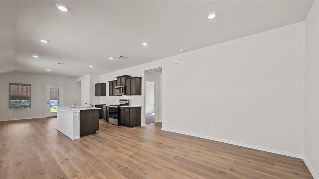 Wood-finish flooring, recessed lighting, vaulted ceiling, kitchen island with sink, and dark cabinetry