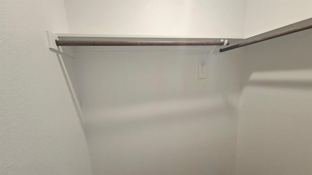 Walk-in closet featuring white painted walls, corner shelving, and multiple clothing rods