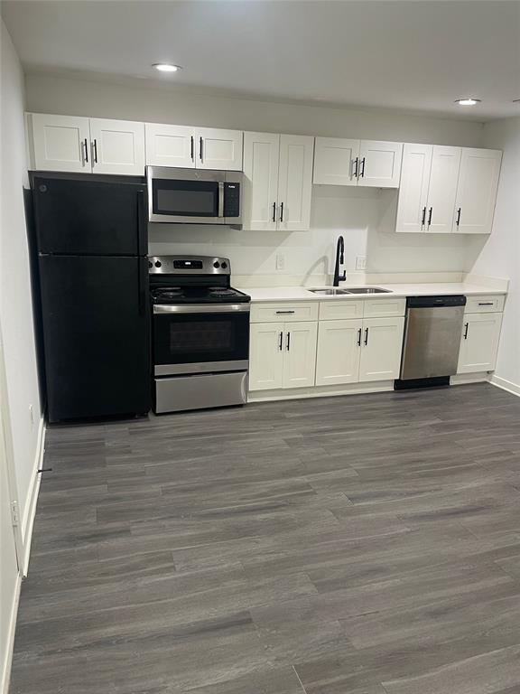 Kitchen featuring white shaker cabinetry, stainless steel appliances, a black refrigerator, light-toned countertops, and wood-finish flooring