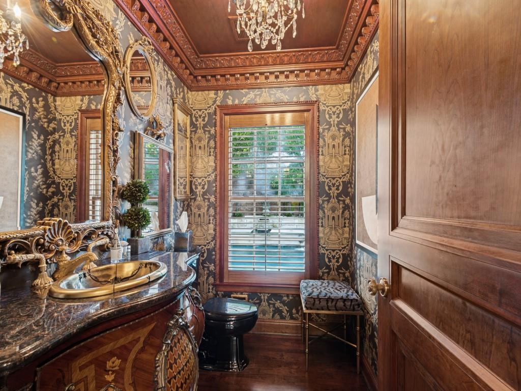 Ornate vanity with dark polished stone countertop, decorative metal drop-in sink, intricate wood-paneled door, elaborate crown molding, and custom wood window shutters