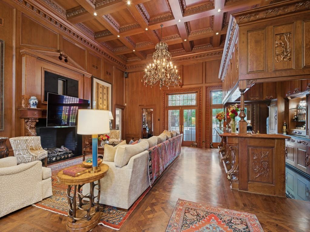 Wood-paneled room featuring a coffered ceiling, herringbone hardwood flooring, an ornate built-in bar, a fireplace with carved detailing, and a multi-tiered metal chandelier