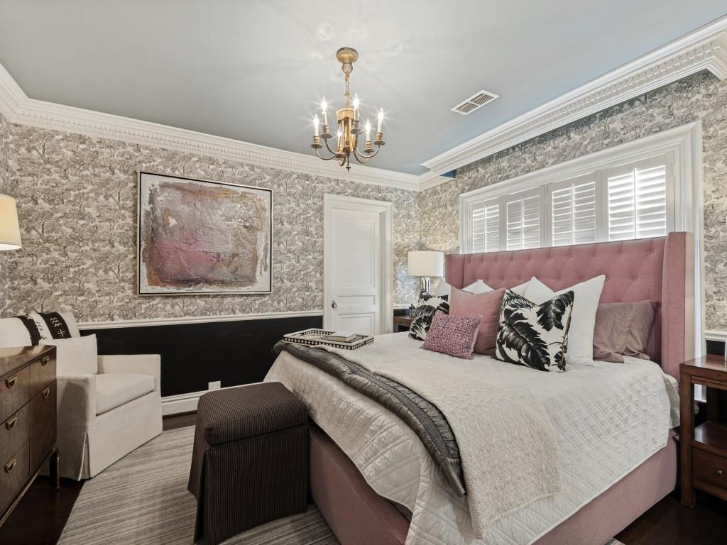 Bedroom featuring detailed crown molding, floor-to-ceiling patterned wall coverings, shutter-style window treatments, and a hanging metal chandelier