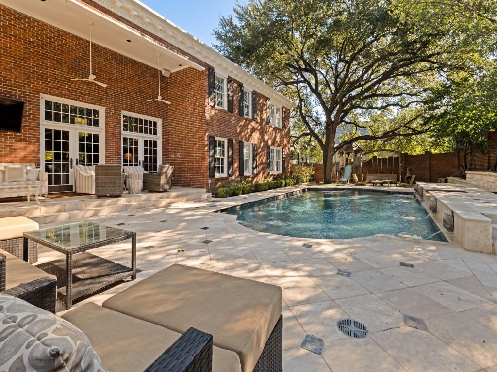 Custom brick exterior featuring a covered patio, limestone-paved terrace, inground pool with water features, and mature trees