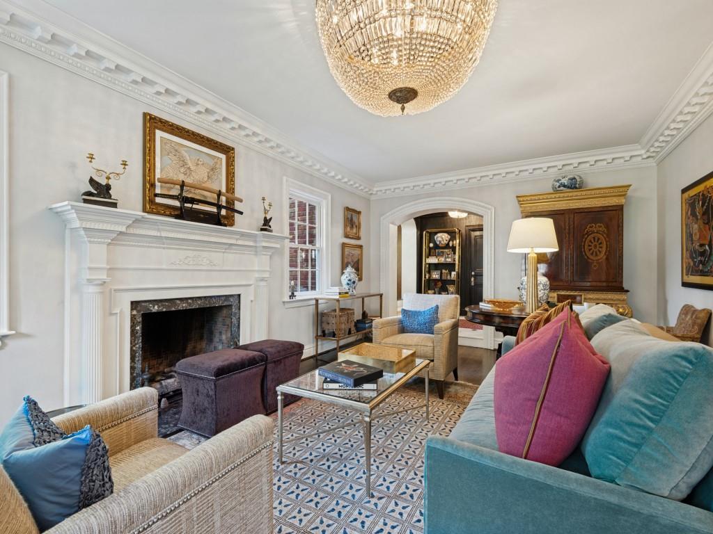 Living room featuring a detailed fireplace mantel, crown molding, arched entry, and a crystal chandelier