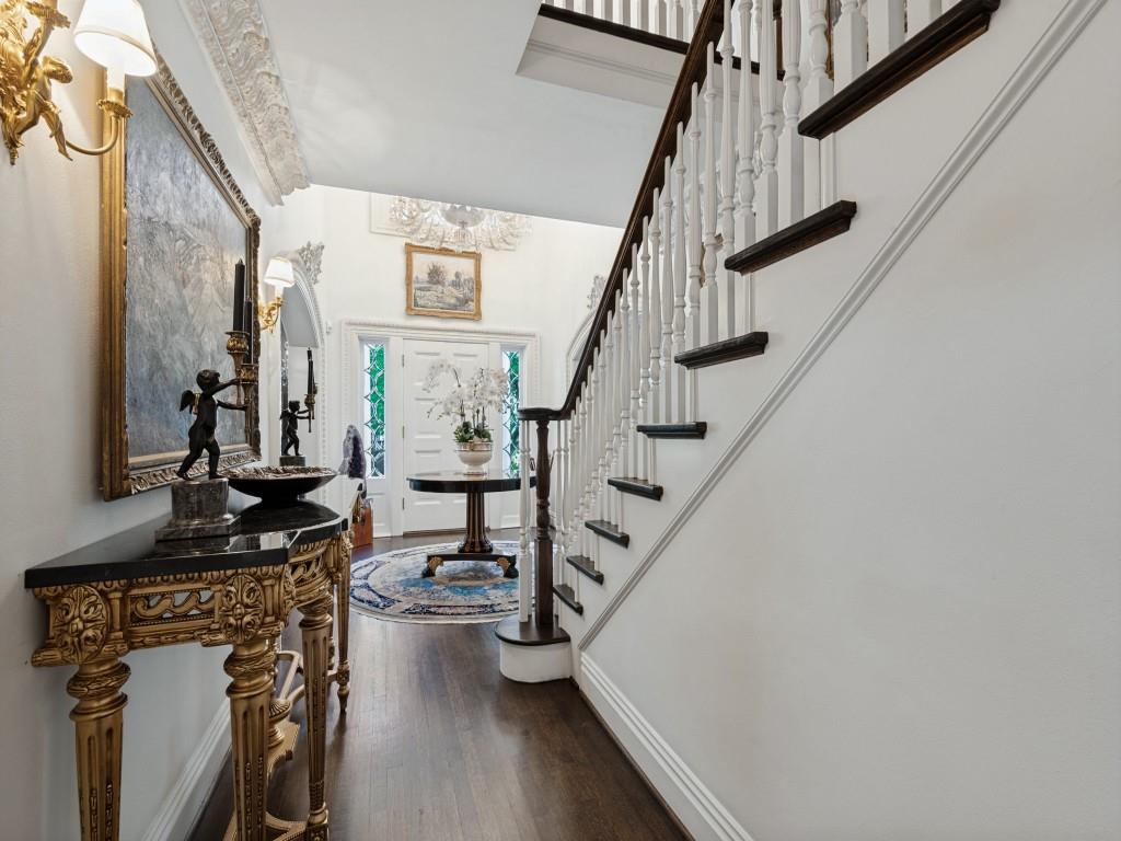 Foyer featuring wood-finish flooring, a staircase with white balusters and dark-toned treads, intricate crown molding, and an arched entry door with sidelights Foyer featuring wood-finish flooring, a staircase with white balusters and dark-toned treads, intricate crown molding, and an arched entry door with sidelights