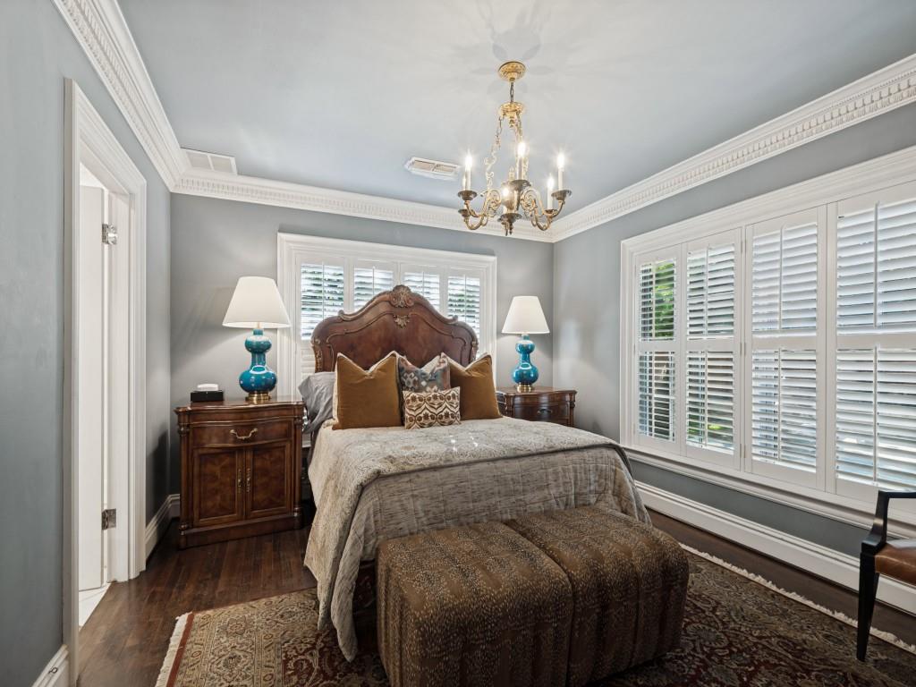 Bedroom featuring wood-finish flooring, intricate crown molding, white plantation shutters, and a classic metal chandelier