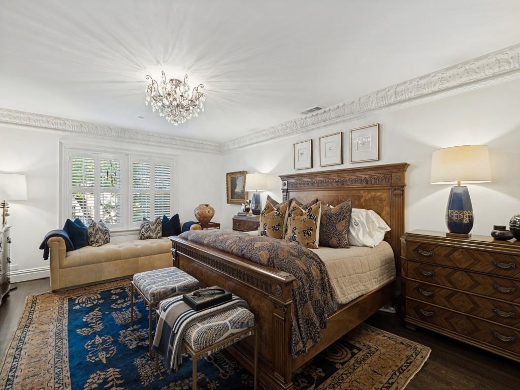 Intricate crown molding, crystal chandelier, and shuttered windows featuring wood-finish flooring