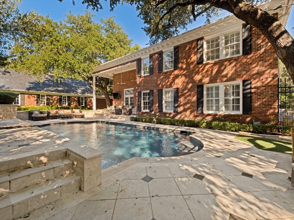 Brick exterior featuring a covered patio, stone pool decking, and an in-ground swimming pool