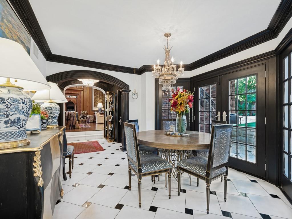 Dining space featuring oversized white floor tiles with black accent squares, contrasting black crown molding, arched entryways, and double glass-paneled doors with black trim