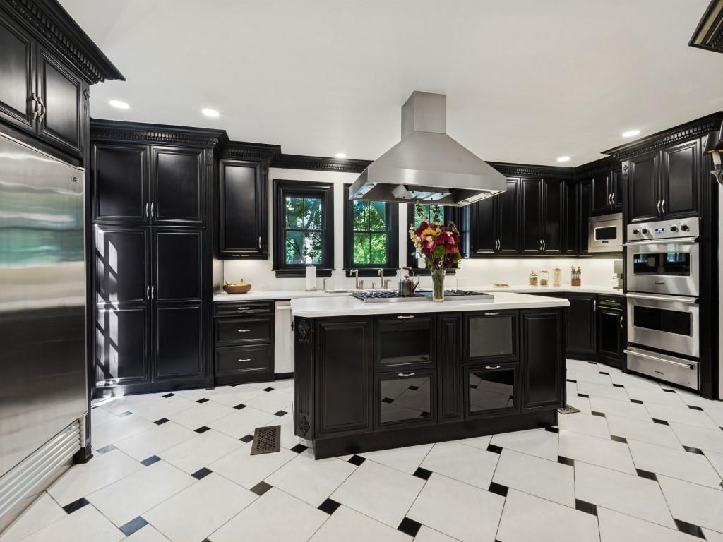 Kitchen featuring custom black cabinetry, a central island with a contrasting stone countertop, stainless steel appliances, a stainless steel range hood, and tile flooring with a geometric pattern