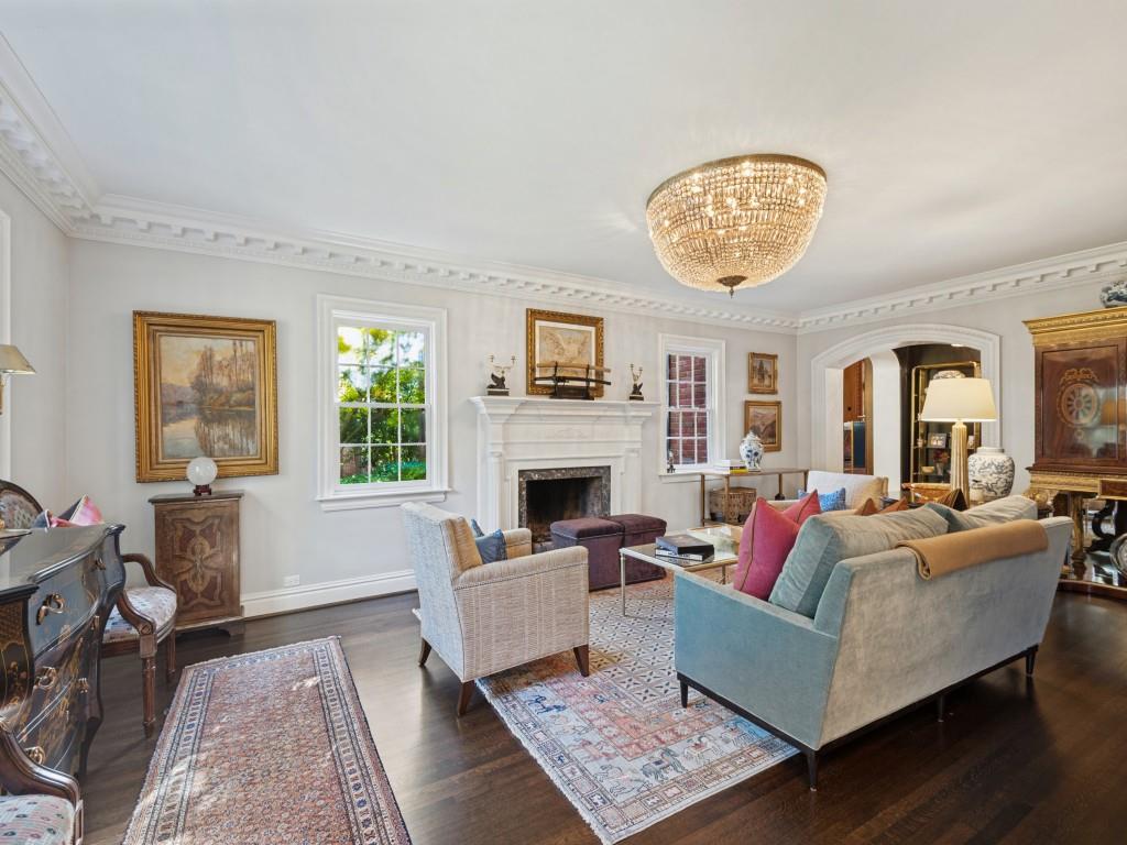 Living space featuring dark wood-finish flooring, crown molding, a central crystal chandelier, and a masonry fireplace with a white mantel