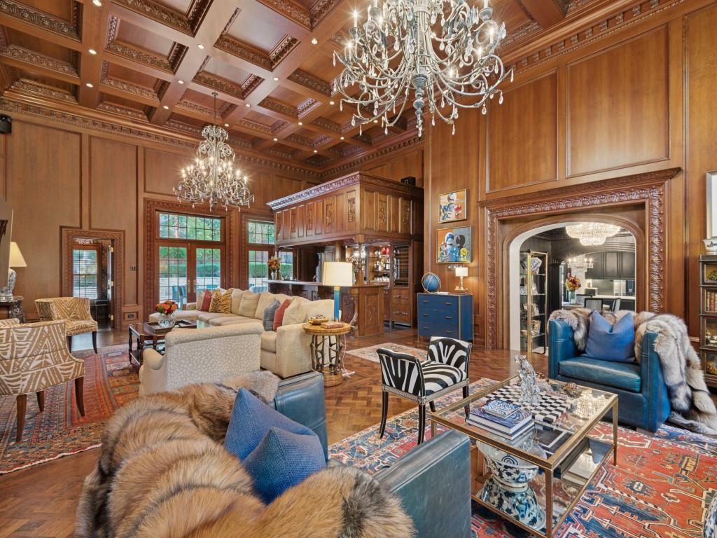 Grand room featuring extensive wood-paneled walls, a coffered ceiling with intricate detailing, polished herringbone wood-finish flooring, two large crystal chandeliers, and a custom built-in bar