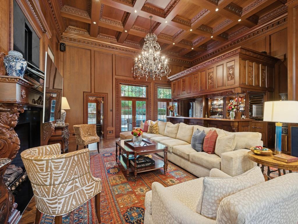 Custom wood-paneled walls, coffered ceilings with intricate crown molding, carved wood fireplace surround, full-length built-in bar, and glass-paneled double doors Custom wood-paneled walls, coffered ceilings with intricate crown molding, carved wood fireplace surround, full-length built-in bar, and glass-paneled double doors