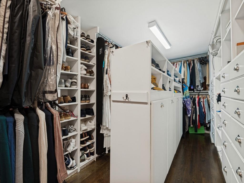 Custom walk-in closet featuring extensive white built-in cabinetry, floor-to-ceiling shelving, integrated drawer stacks, and dark wood-finish flooring