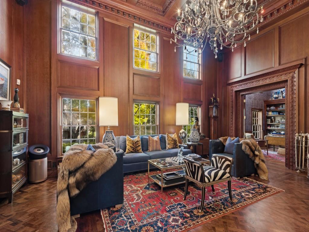 Two-story room featuring floor-to-ceiling wood paneling, herringbone-patterned wood flooring, an ornate multi-tiered crystal chandelier, and deep crown molding