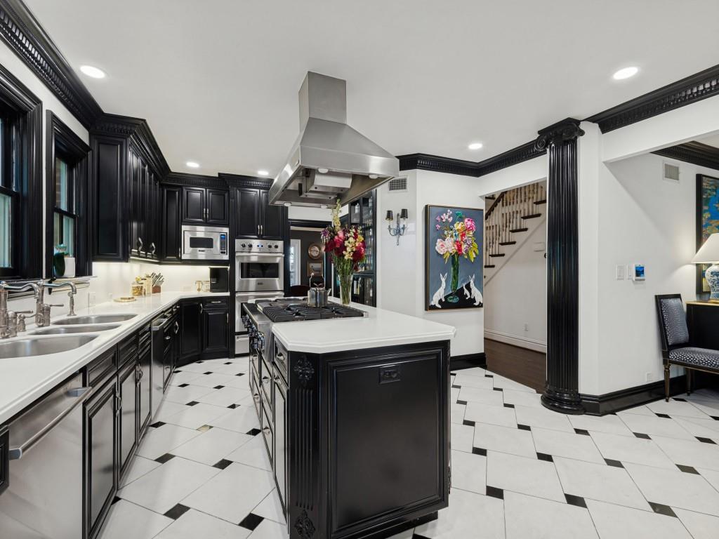 Kitchen featuring custom black cabinetry, a central island with a gas cooktop, white solid-surface countertops, stainless steel range hood, and black-and-white diamond pattern tile flooring