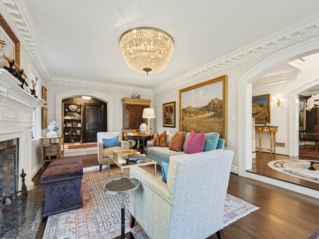 Living room featuring ornate crown molding, a central crystal chandelier, a stone-surround fireplace, arched entryways, and wood-finish flooring