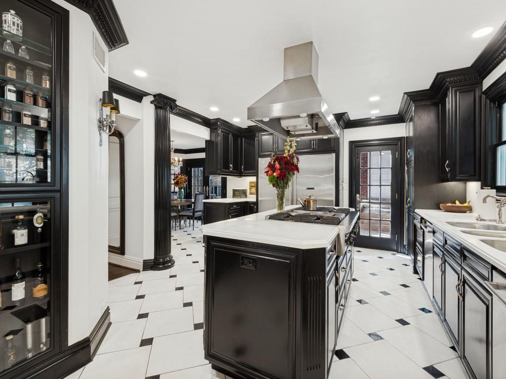 Kitchen featuring custom black cabinetry, central island with gas cooktop, stainless steel ventilation hood, stone countertops, and geometric tile flooring