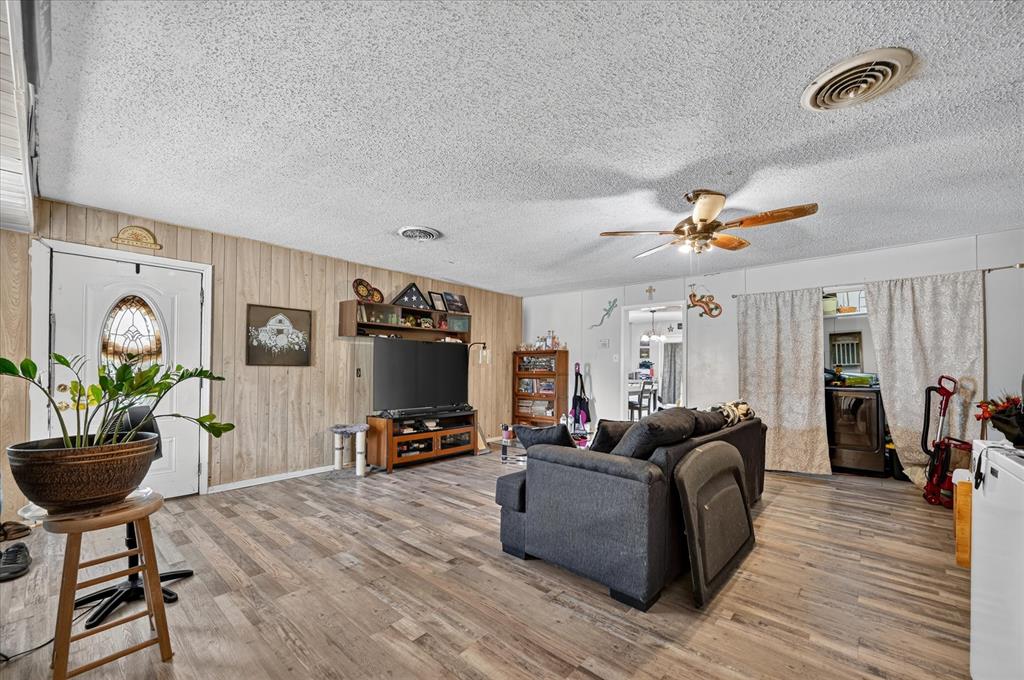Wood-finish flooring throughout, white paneled entry door with an oval stained-glass insert, and a ceiling fan with integrated lighting