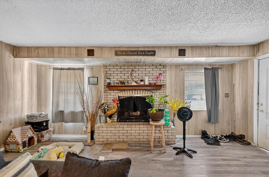 Brick fireplace with wood mantel, plank wood-finish flooring, wood paneling, and an exterior door