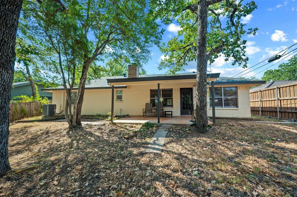 Exterior featuring a covered patio, brick chimney, privacy fencing, and mature trees