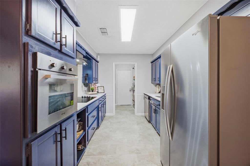 Galley kitchen featuring blue cabinetry, stainless steel appliances, a built-in oven, and light-toned flooring
