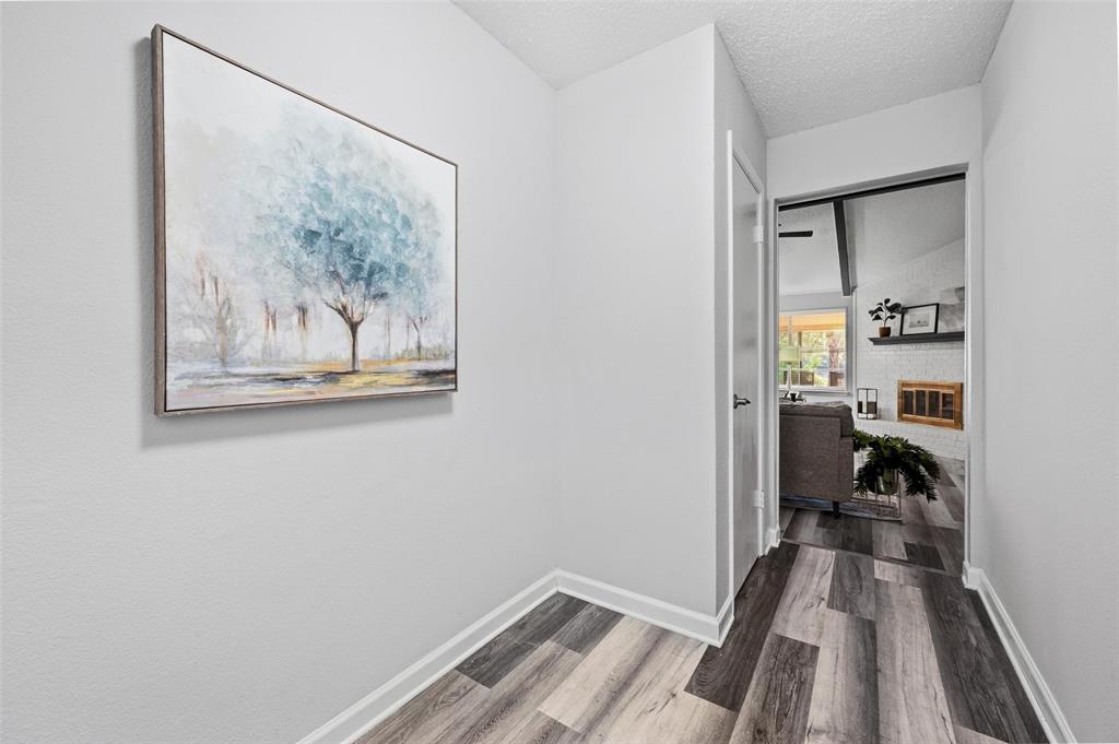 Wood-finish flooring with white trim, leading to an interior doorway with a black door handle, revealing a white brick fireplace with a wood mantel