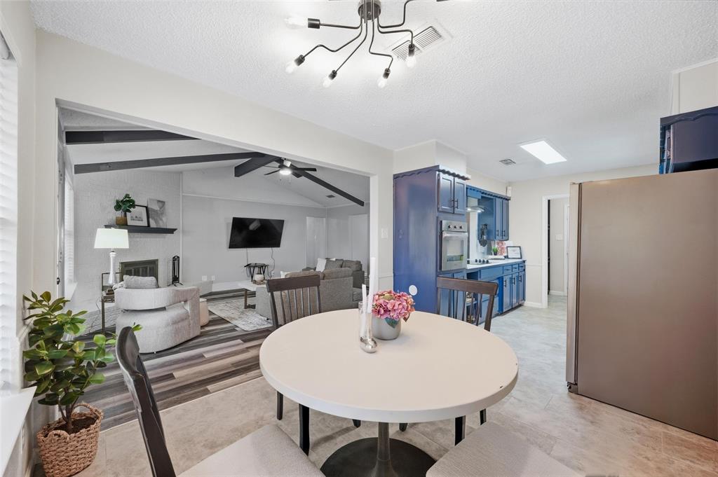 Open-concept layout featuring a kitchen with blue cabinetry and stainless steel appliances, a dining area, and a living space with vaulted ceilings and a fireplace