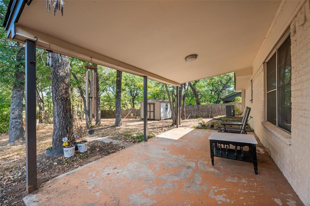 Covered concrete patio with overhead lighting, featuring a brick exterior wall and a detached shed in the background