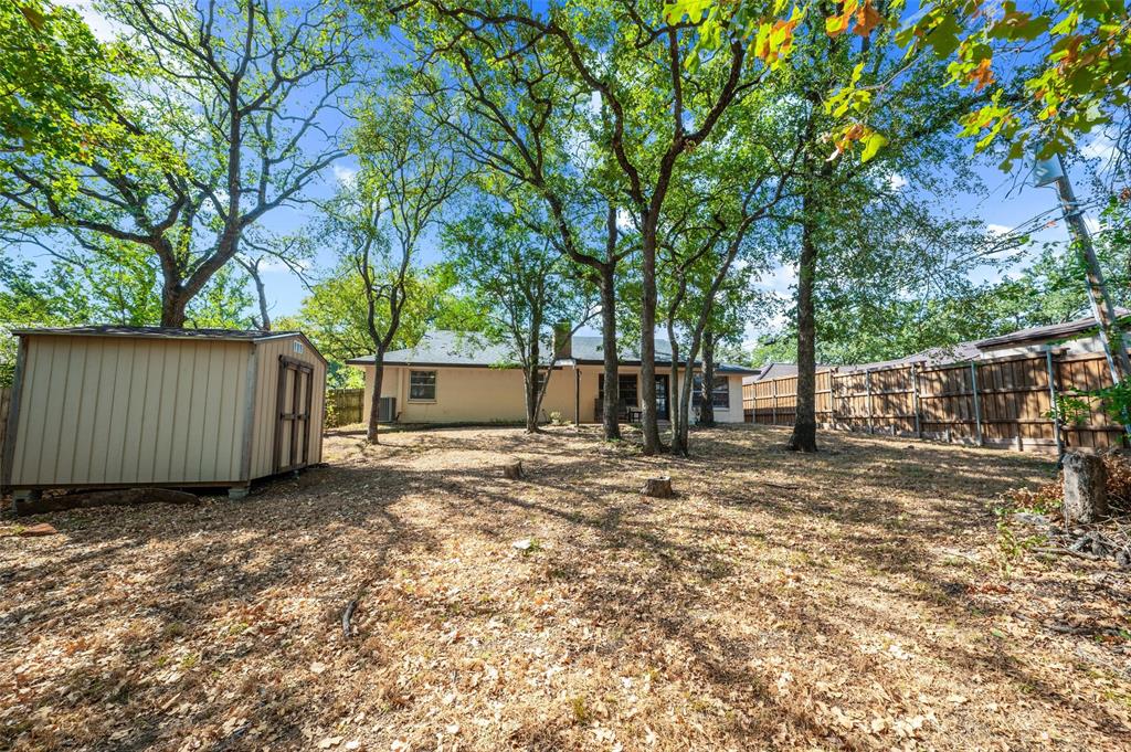 Expansive rear yard featuring mature trees, a detached storage shed, and perimeter fencing