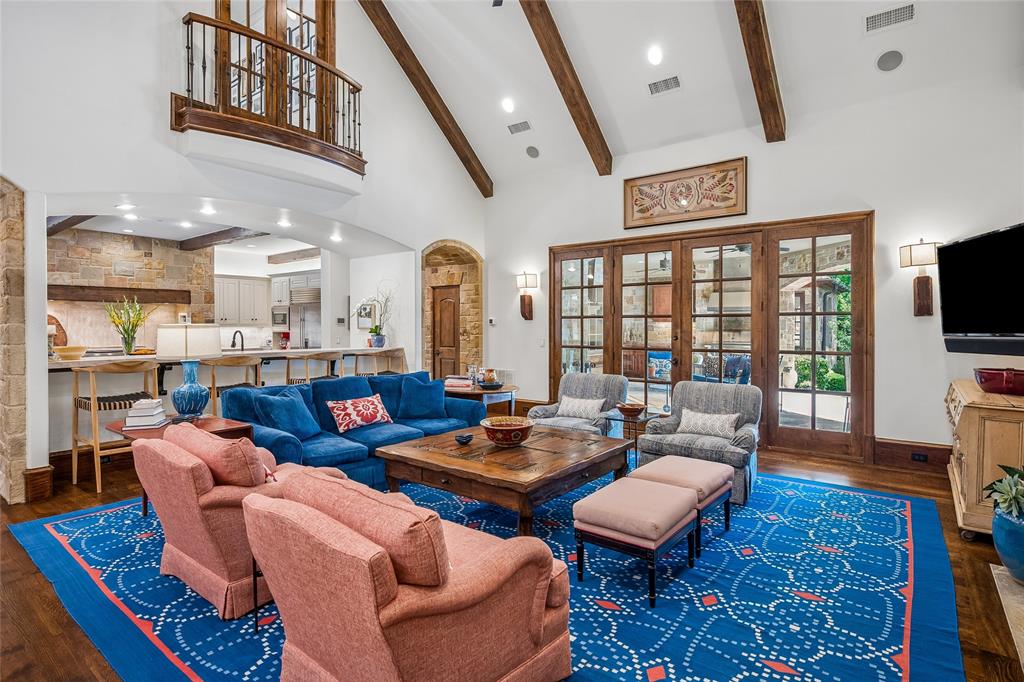 Vaulted ceiling with exposed wood beams, wood-finish flooring, a Juliet balcony with wrought iron railing, and wood-framed French doors