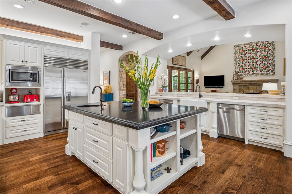 Open to the great room, kitchen features hardwood flooring, white cabinetry, stainless steel appliances, dark countertop on kitchen island, and a built-in kitchen island with shelving Open to the great room, kitchen features hardwood flooring, white cabinetry, stainless steel appliances, dark countertop on kitchen island, and a built-in kitchen island with shelving