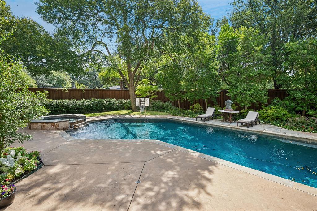 Expansive backyard featuring a rectangular swimming pool, stone-clad spa with waterfall, concrete patio, and privacy fencing Expansive backyard featuring a rectangular swimming pool, stone-clad spa with waterfall, concrete patio, and privacy fencing