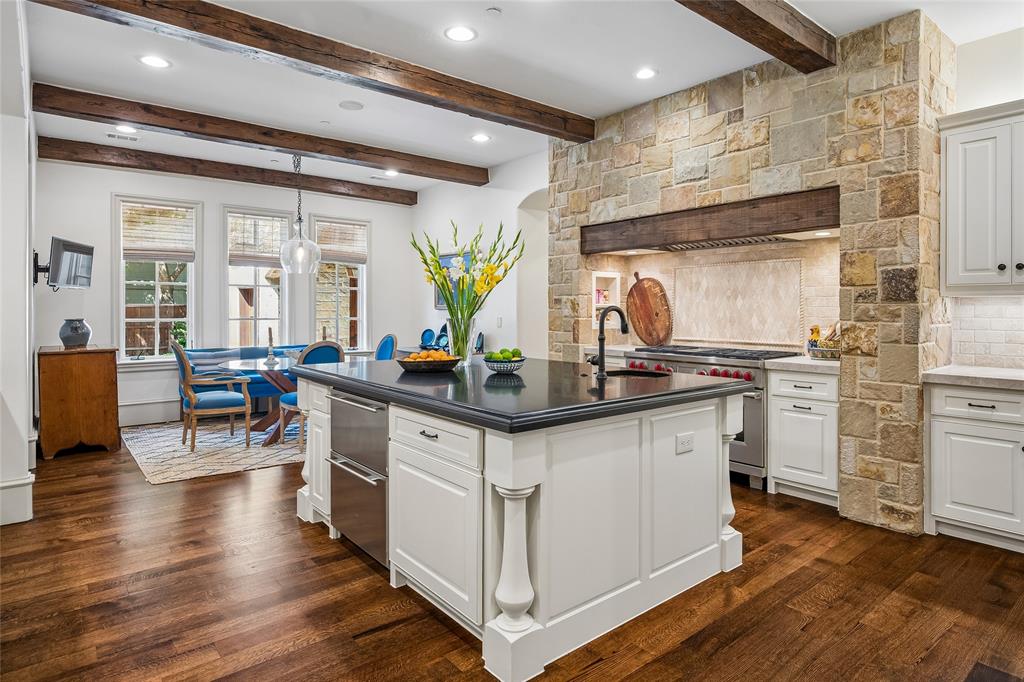 Gourmet kitchen featuring a stone-clad range hood, wood-beamed ceiling, wood-finish flooring, white cabinetry, and a center island with a dark countertop