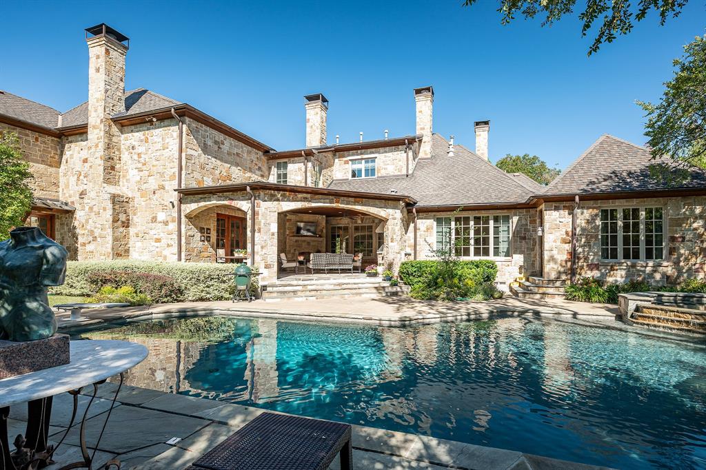 Stone exterior residence featuring multiple chimneys, a covered outdoor living area, and a swimming pool with stone hardscaping Stone exterior residence featuring multiple chimneys, a covered outdoor living area, and a swimming pool with stone hardscaping