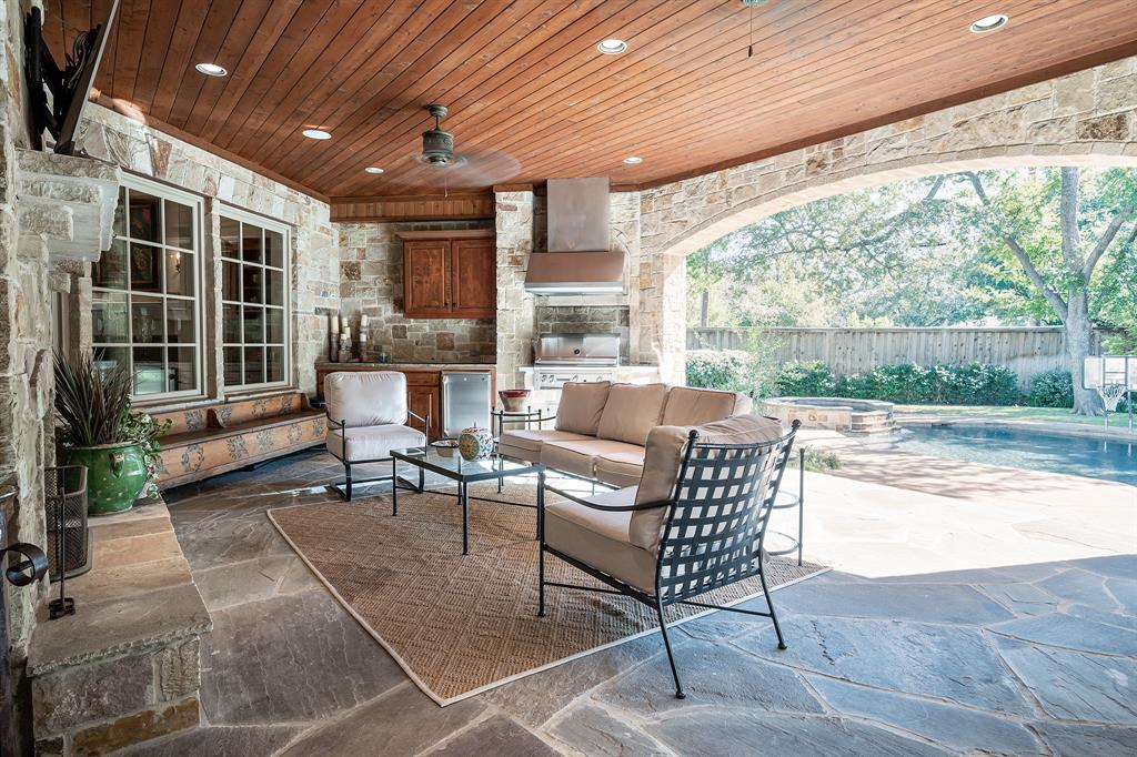 Covered outdoor living space featuring flagstone flooring, a natural stone fireplace, recessed lighting, and a built-in outdoor kitchen with wooden cabinetry