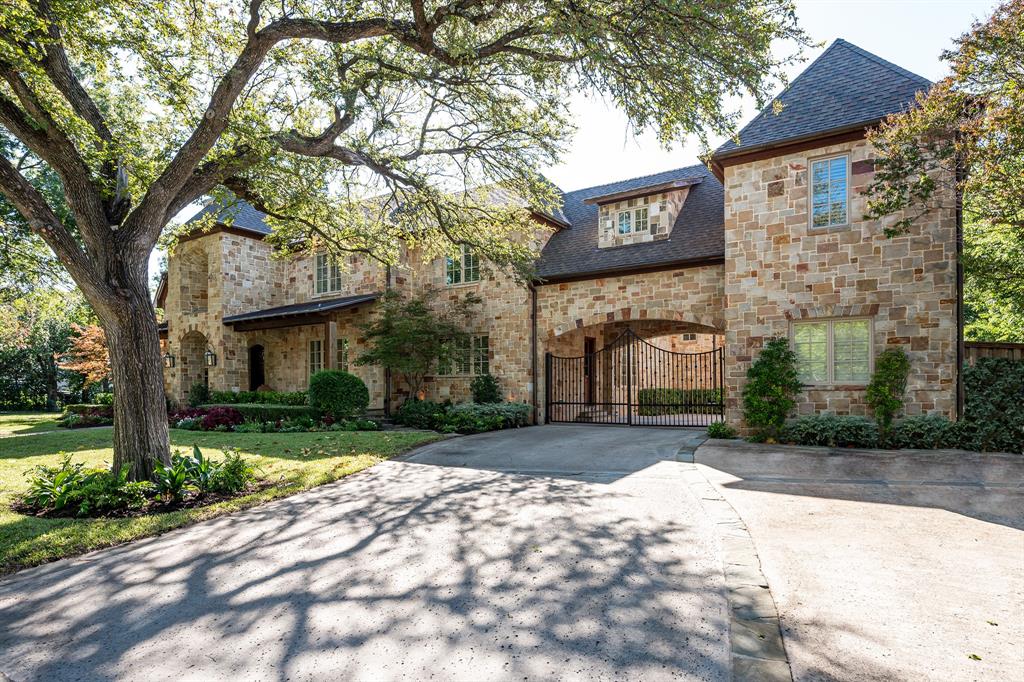Stone exterior façade featuring a multi-gabled roofline, arched portico, gated motor court, and mature landscaping Stone exterior façade featuring a multi-gabled roofline, arched portico, gated motor court, and mature landscaping
