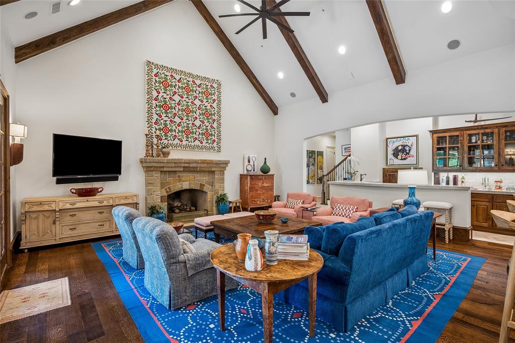 Vaulted ceiling with exposed wood beams, stone-clad fireplace, wood-finish flooring, recessed lighting, and a built-in wet bar with cabinetry