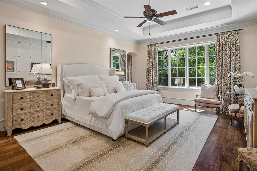 First floor primary bedroom. Hardwood flooring, tray ceiling with recessed lighting, ceiling fan, and large windows with transom panes
