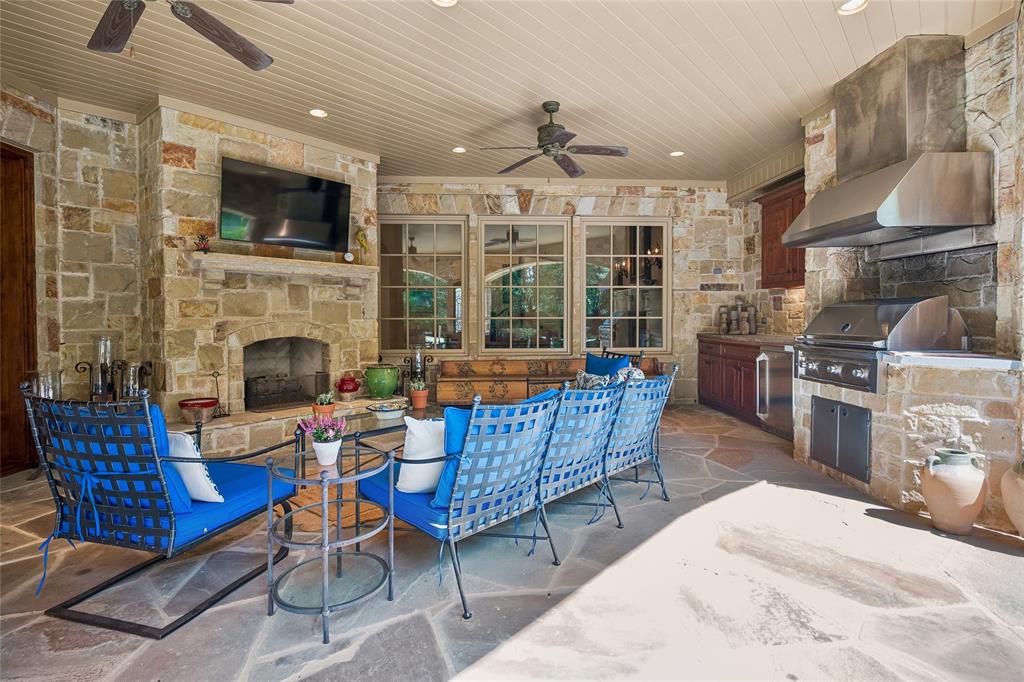 Covered patio featuring a stone fireplace, built-in outdoor grill, integrated range hood, and planked ceiling with recessed lighting