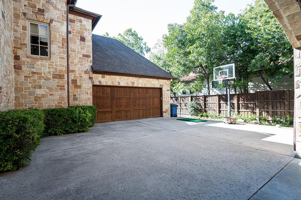 Stone veneer exterior, multi-car garage with wood-finish doors, expansive concrete driveway, and cedar privacy fencing
