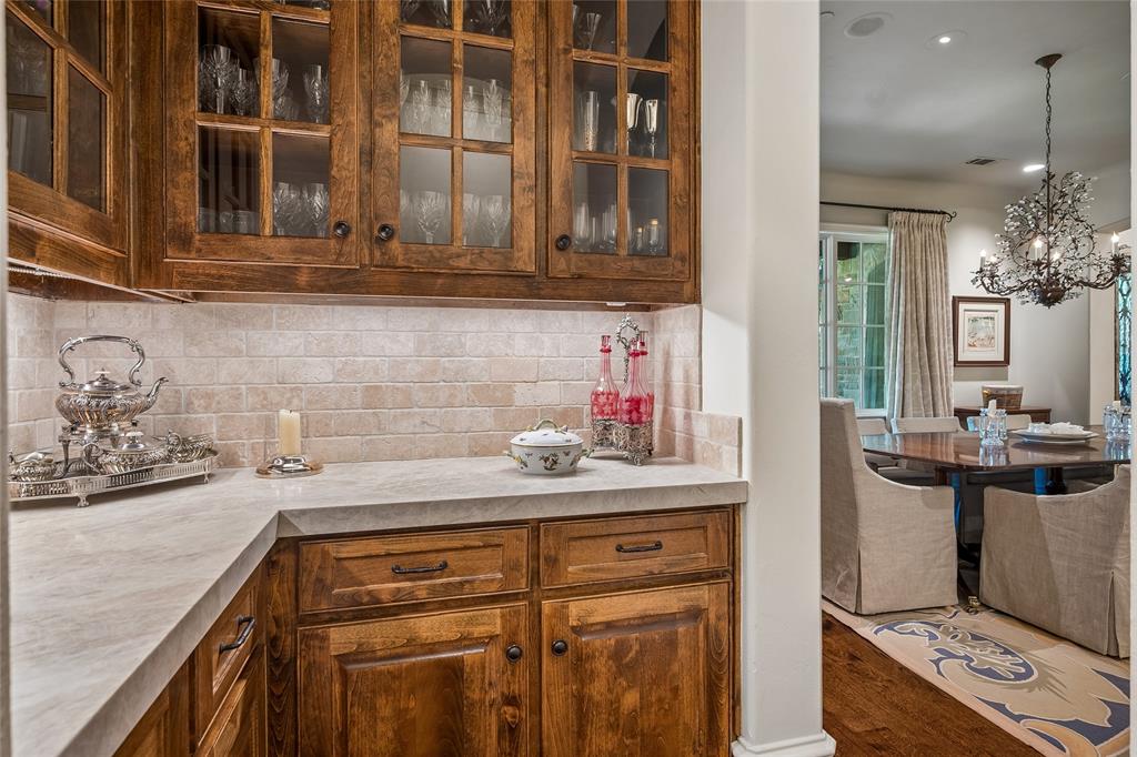 Rich wood-finish cabinetry with glass panel inserts, light-toned countertop, and tiled backsplash
