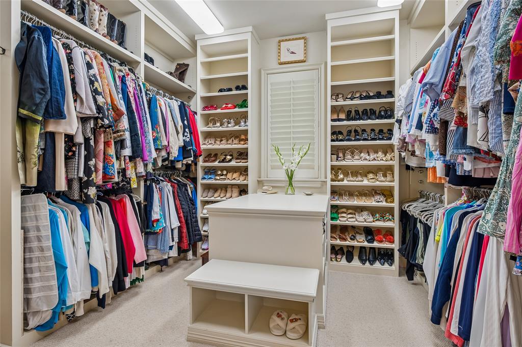 His-n-Her primary closets with built-in shelving, extensive hanging storage, central island with integrated seating, window with plantation shutters, and recessed lighting fixtures