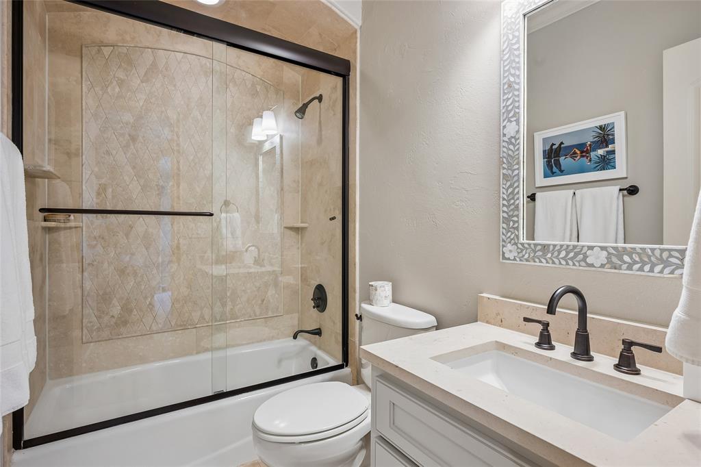 Bathtub with glass sliding doors, tiled surround with decorative inlay, and matte black fixtures