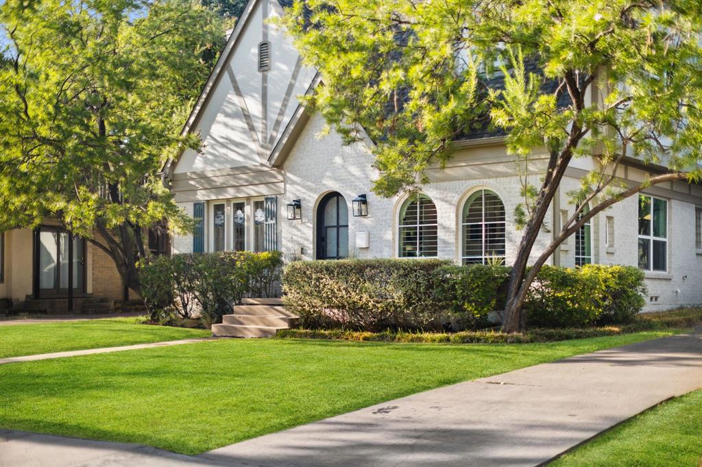 Tudor-style architecture featuring a prominent gable, arched entry, decorative stucco facade, and established landscaping