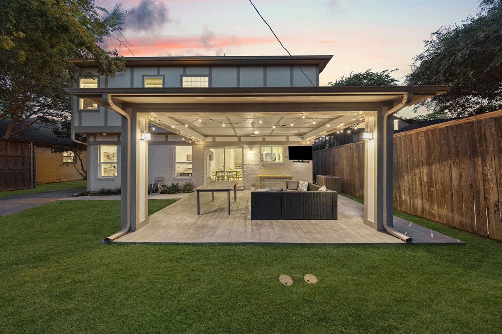 Expansive rear yard featuring a covered patio, string lighting, and wood-finish decking